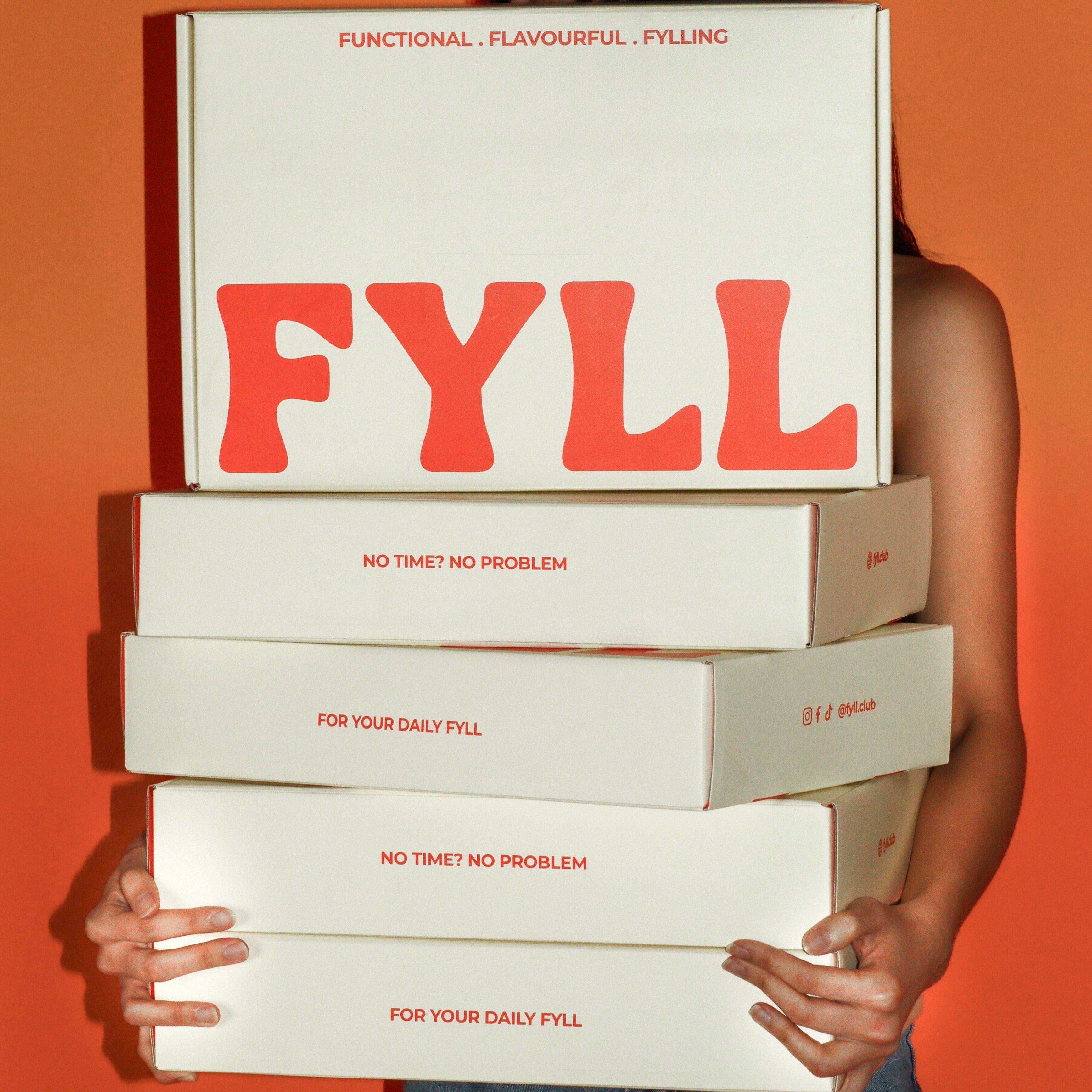 Person holding a stack of 'Fyll' boxes against an orange background